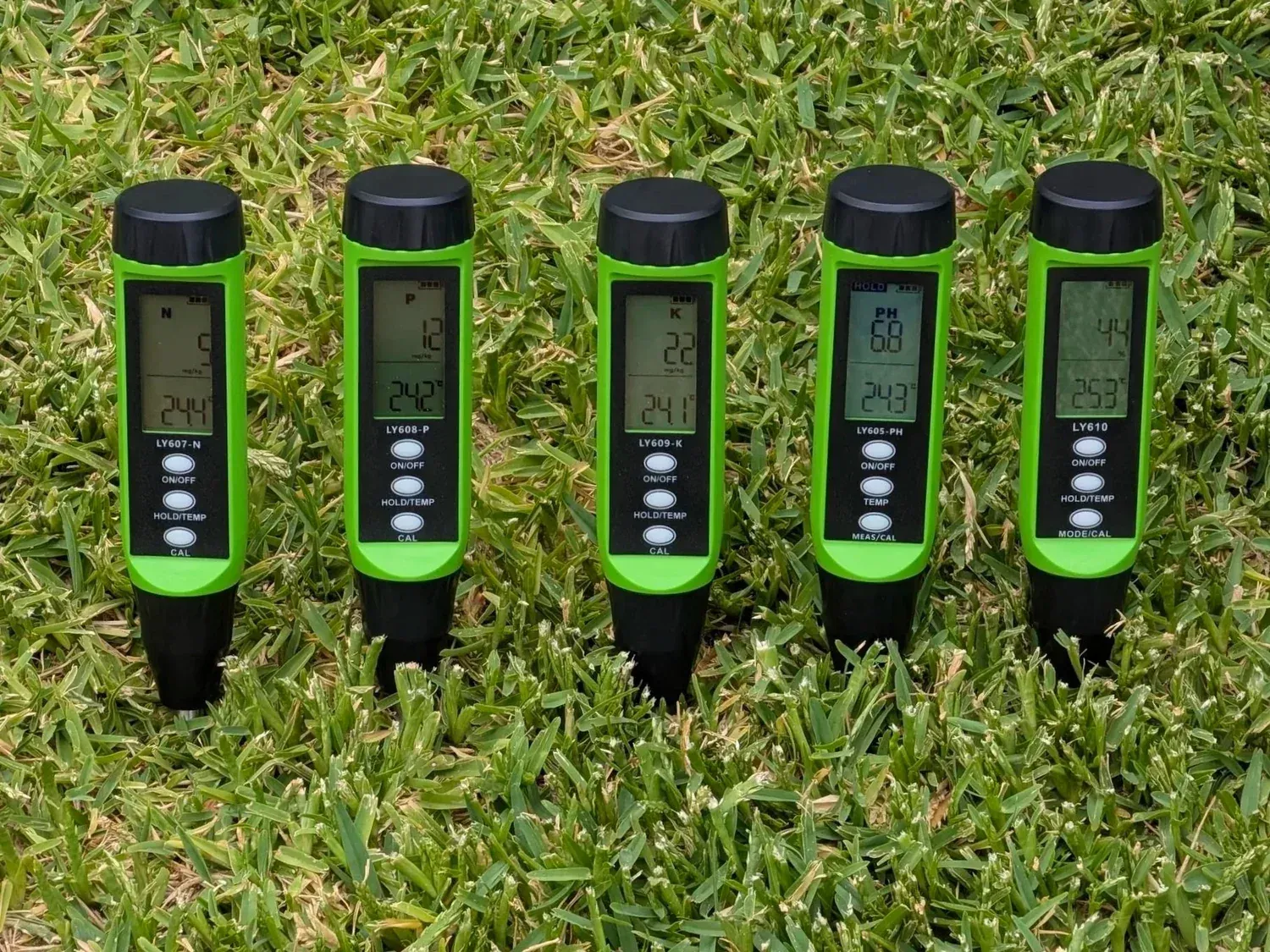 The five Field Spears soil testing spears, green and black with LCD screens and buttons, standing upright in grass